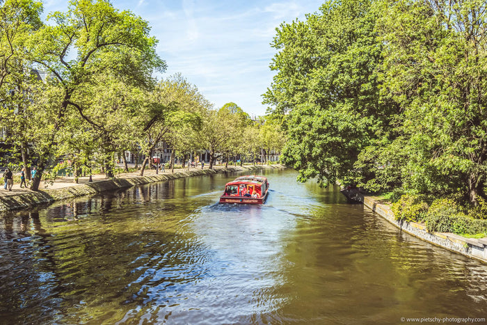 Amsterdam canal cruise in spring, Amsterdam canals spring, spring in Amsterdam photography, canal boat Amsterdam, blooming trees Amsterdam canals, Amsterdam cityscape spring, peaceful Amsterdam waterways, Netherlands spring travel photography, fine art Am