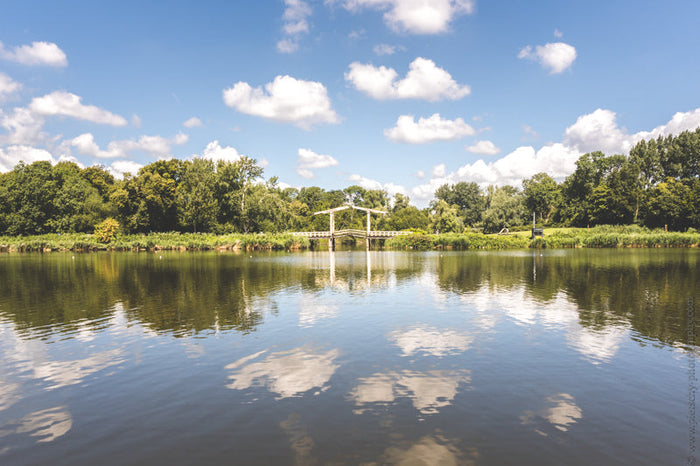 Amsterdamse Bos Amsterdam, serene landscape featuring a calm lake with reflections of the blue sky and clouds, surrounded by dense trees and greenery. Captured by Stefanie Pietschmann, professional photographer.