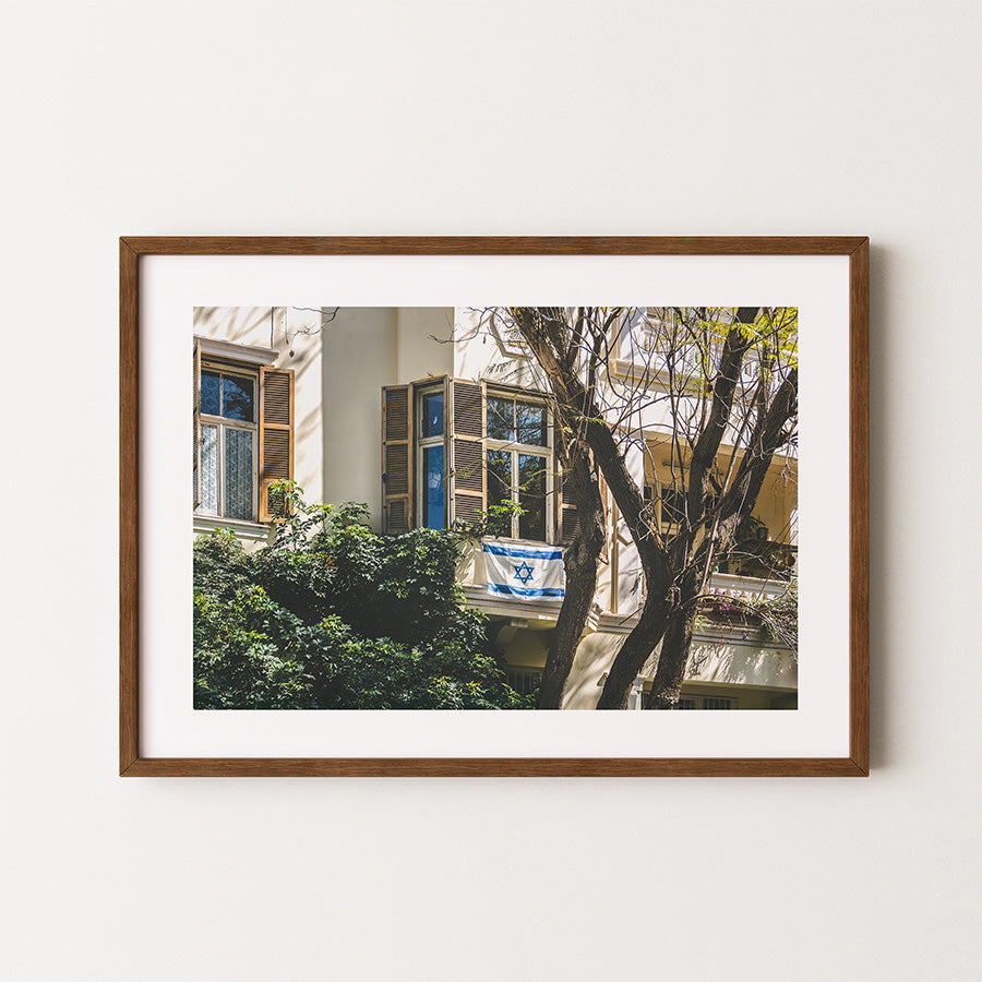 This Tel Aviv Israeli flag wall art captures a quiet moment of city life, where open shutters, soft light, and the Magen David on a balcony come together in a scene full of heritage and warmth. A fine art print that adds meaning, calm, and architectural charm to any space.