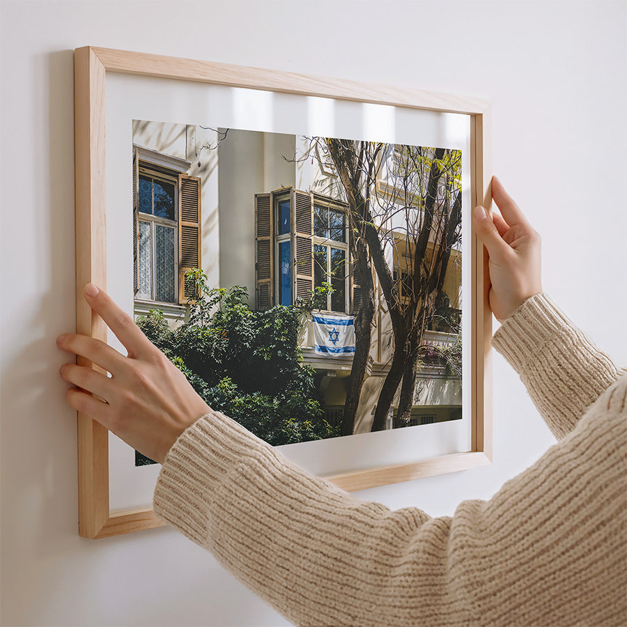 This Tel Aviv Israeli flag wall art captures a quiet moment of city life, where open shutters, soft light, and the Magen David on a balcony come together in a scene full of heritage and warmth. A fine art print that adds meaning, calm, and architectural charm to any space.