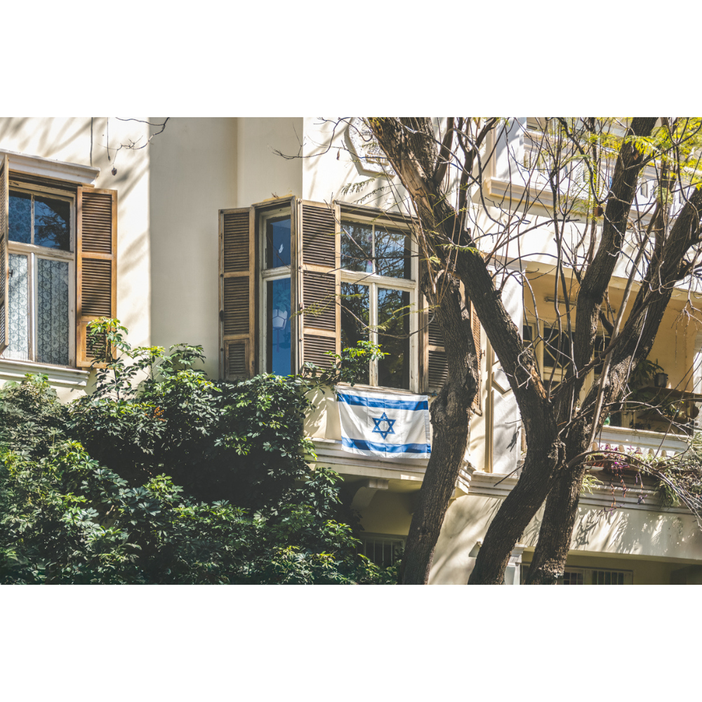 This Tel Aviv Israeli flag wall art captures a quiet moment of city life, where open shutters, soft light, and the Magen David on a balcony come together in a scene full of heritage and warmth. A fine art print that adds meaning, calm, and architectural charm to any space.